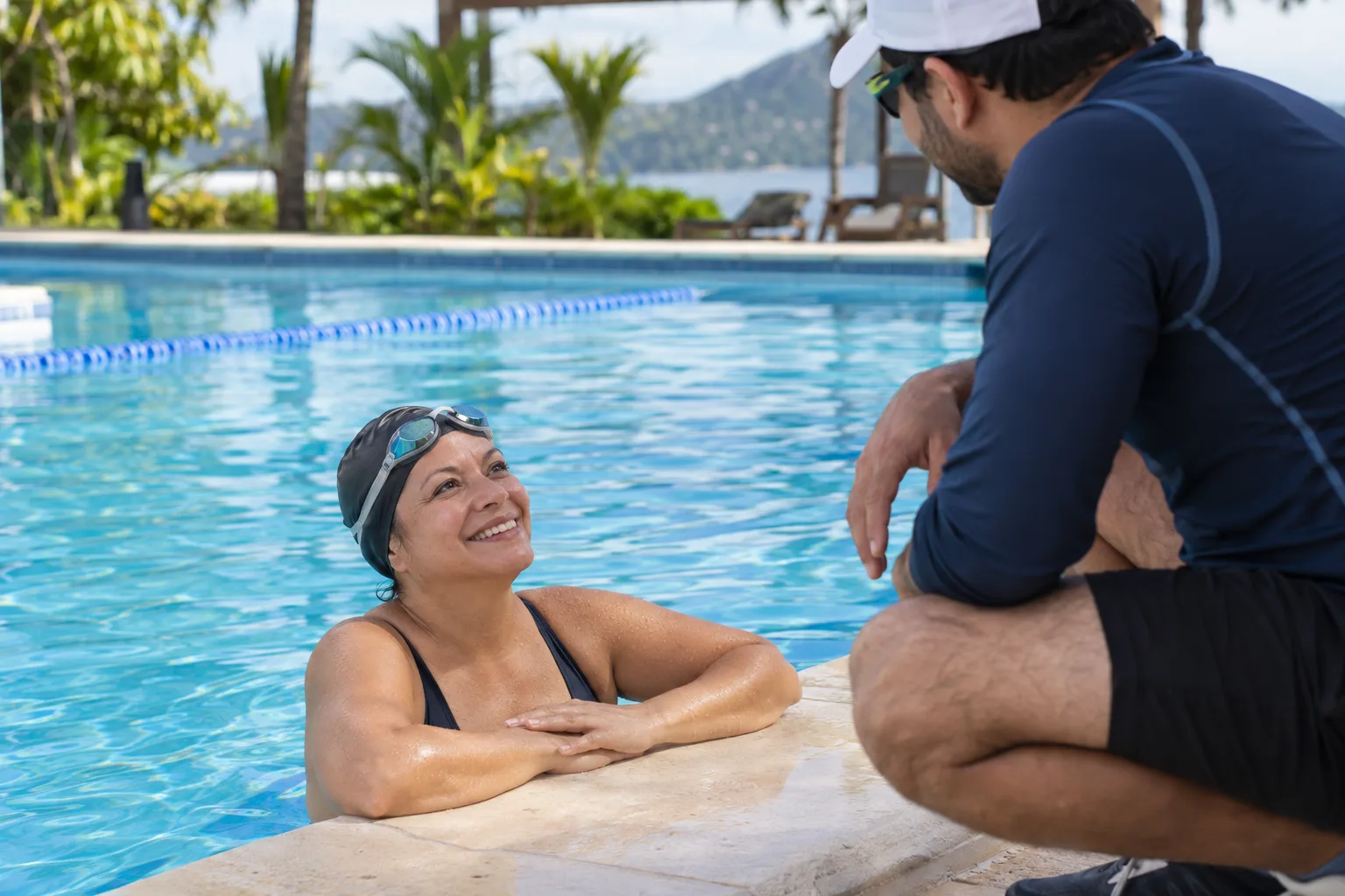Nadadora adulta descansando junto al borde y conversando con su entrenador